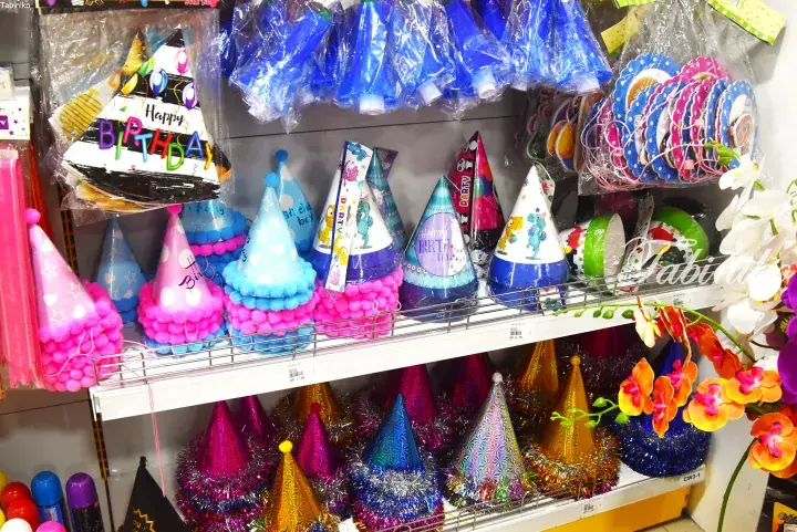 Colorful party hats with pom-poms and tinsel displayed on shelves at a Malaysia store.
