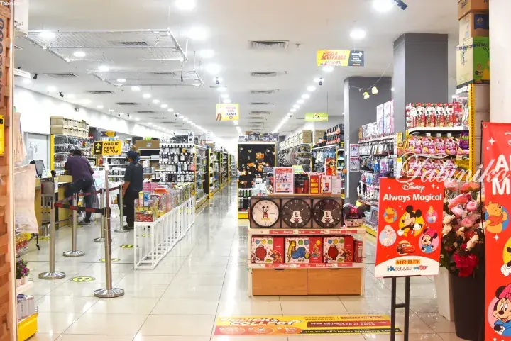 Interior of a MR.DIY store showing aisles of household goods, a checkout counter, and a Disney-themed display stand.