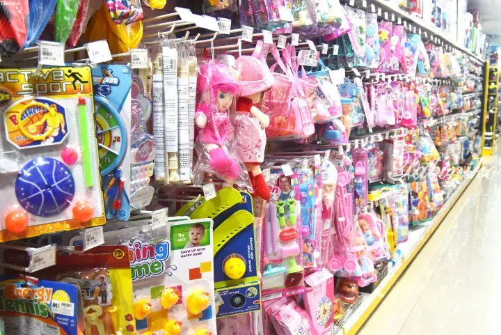 Colorful children’s toys including dolls and sports sets displayed on shelves in a Malaysian store aisle.