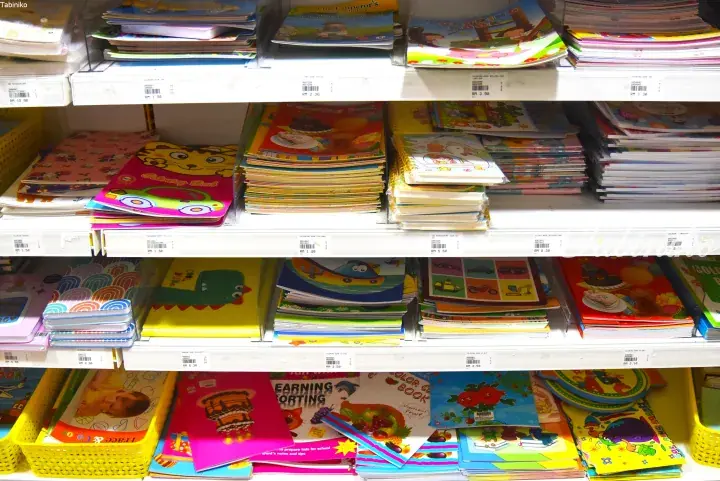 Colorful children’s activity books and notebooks displayed on white shelves with price tags in a Malaysian store.
