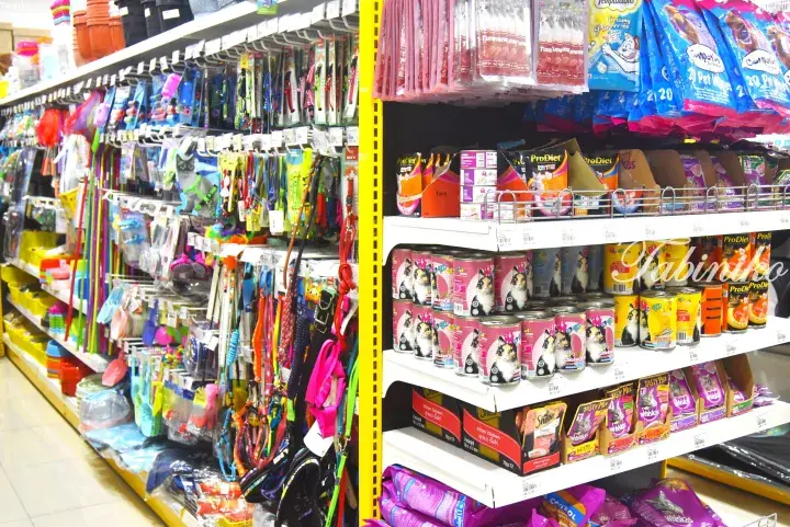 Colorful pet accessories and canned cat food displayed on shelves in a Malaysian pet store.