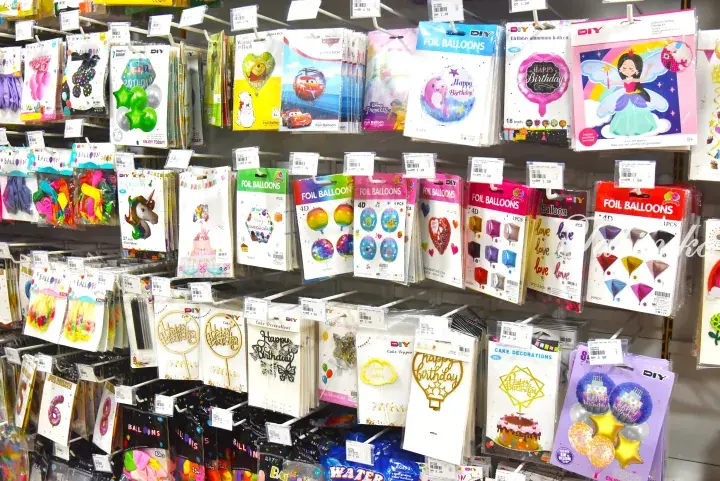 Shelves stocked with colorful foil balloons and cake decorations at a Malaysian party supply store.