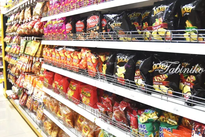 A well-stocked supermarket shelf displaying various snack brands like Lay’s, Jacker, and Skoremi in colorful packaging.