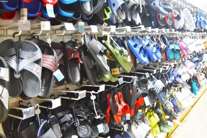 A wall display of colorful men’s sandals and slippers hanging on hooks in a shoe store.