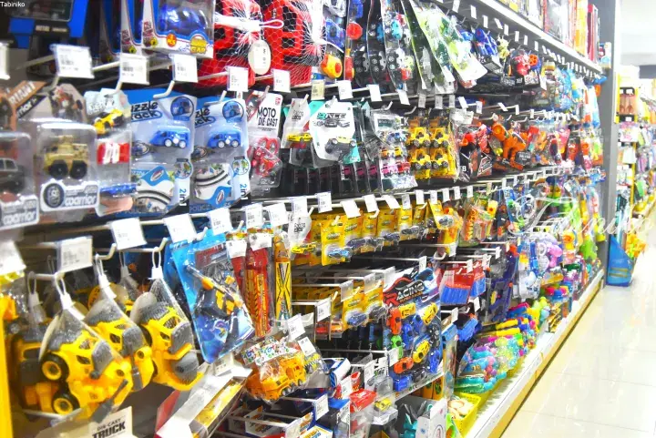Aisle in a Malaysian toy store filled with colorful die-cast cars, construction vehicles, and water guns on shelves.