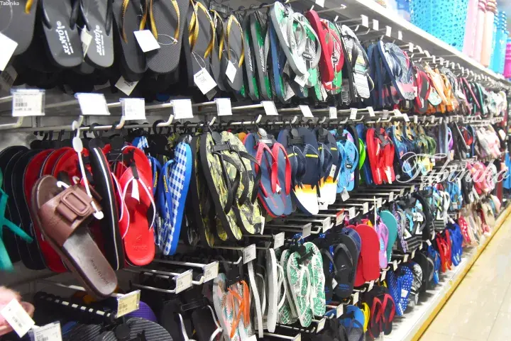 Colorful flip-flops and sandals displayed on a wall rack at a Malaysian retail store.