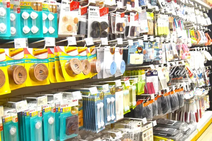 Shelves stocked with DIY household items including furniture leg covers, weather stripping, and safety locks in a Malaysian store.