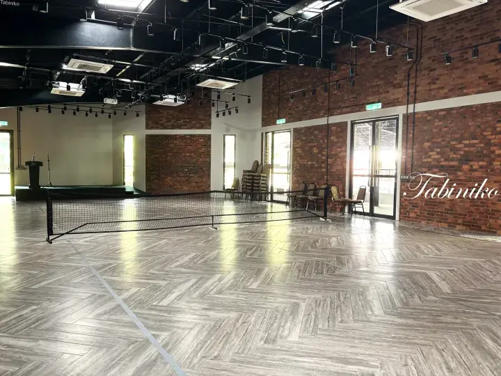 Spacious indoor hall with herringbone flooring, brick walls, and a badminton net setup.
