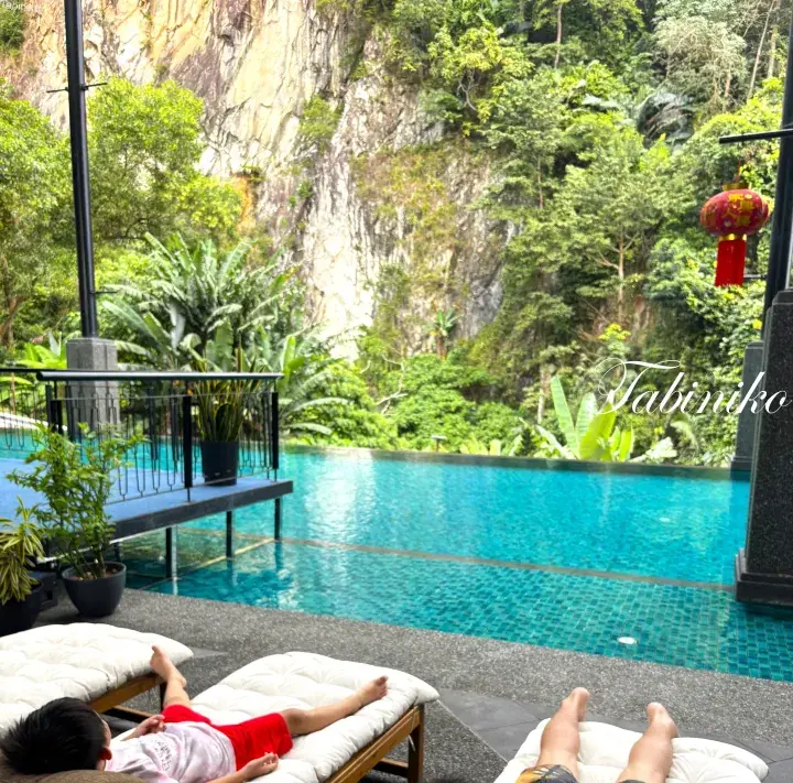 Child relaxing on a sun lounger beside an infinity pool overlooking a lush tropical cliffside at a Malaysian resort.