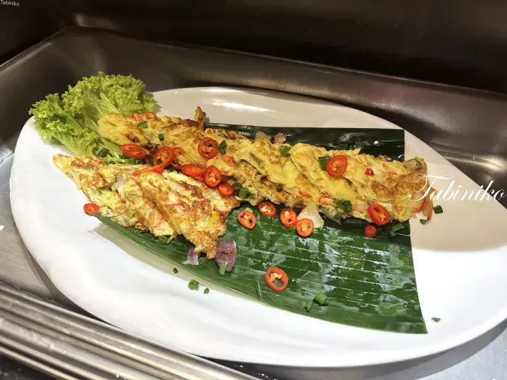 Golden Malaysian omelette garnished with sliced red chilies and green onions, served on a banana leaf.