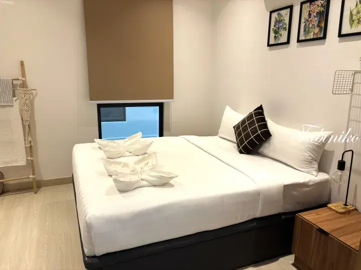 Cozy bedroom with a neatly made bed featuring folded towel swans and a small window overlooking the sea.