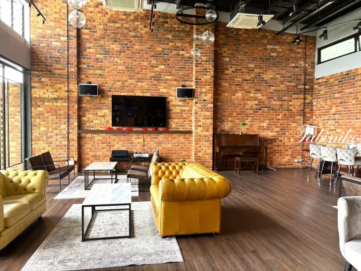 Spacious lounge with exposed brick walls, yellow Chesterfield sofas, and a grand piano in a modern co-working space.