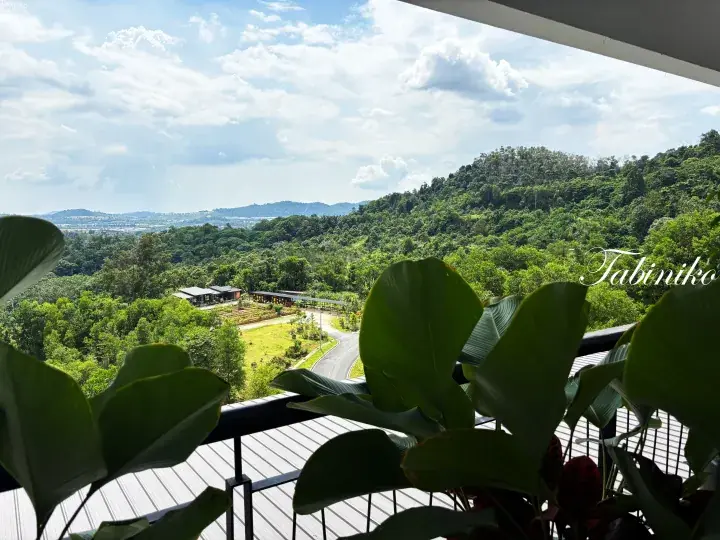 View from a balcony overlooking lush green hills and a winding road in a Malaysian tropical landscape.