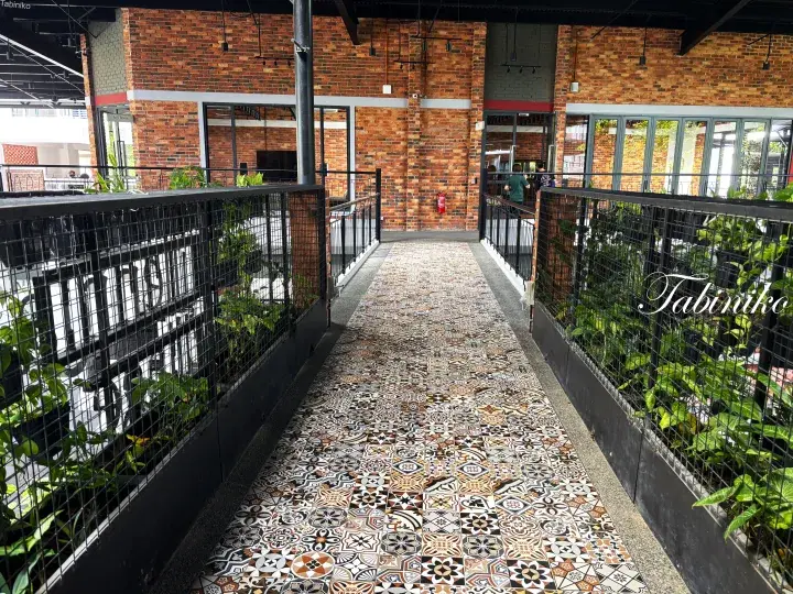 A walkway with patterned tiles and greenery at a modern brick building in Malaysia.