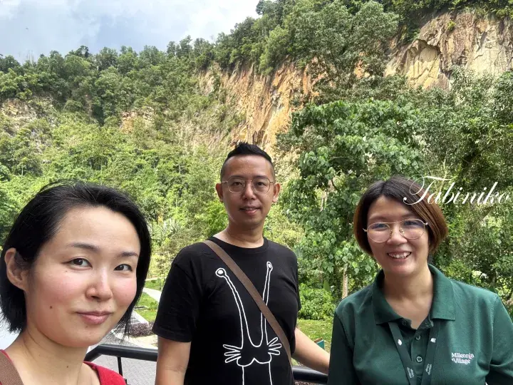 Three people posing for a photo with a lush green hillside and rocky cliff face in the background.