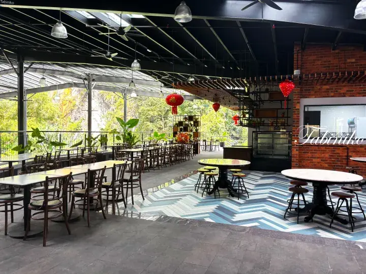 Spacious open-air dining area with wooden tables, chevron-patterned flooring, and red lanterns overlooking lush greenery.