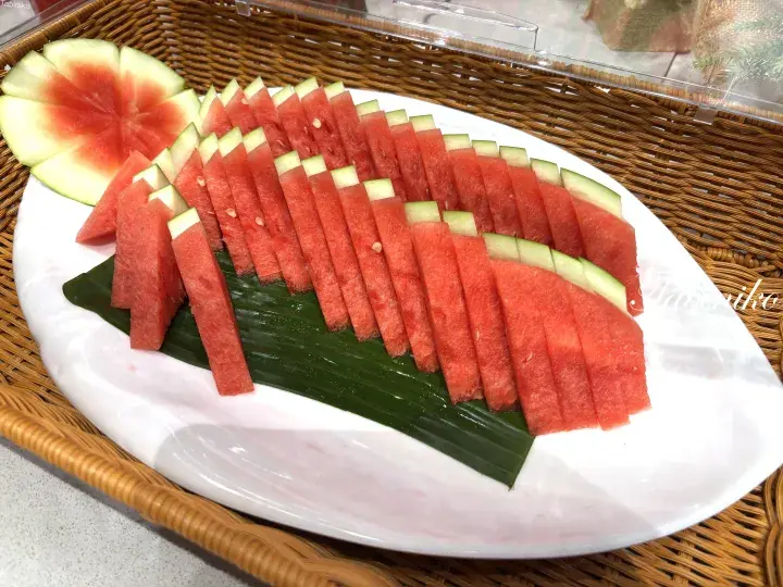 Freshly sliced watermelon arranged on a white platter with a banana leaf, ready to serve.