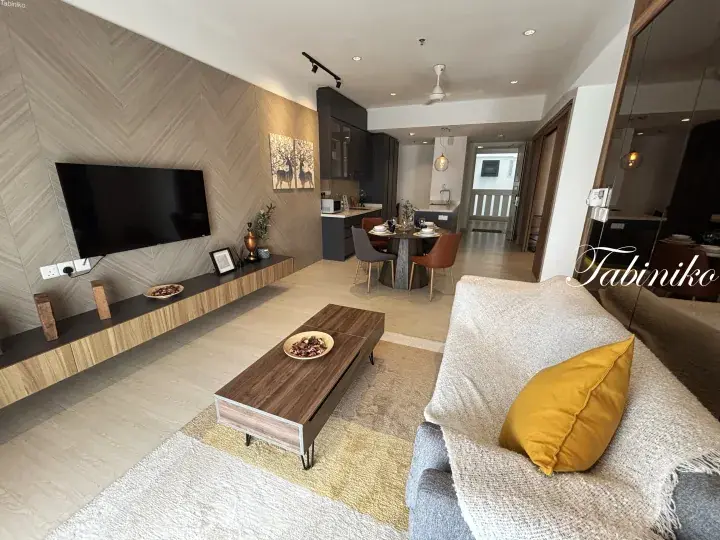 Modern open-plan living room with herringbone wall, floating TV console, and dining area in a Malaysian apartment.