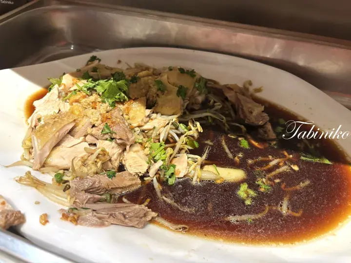 Hainanese chicken rice with tender poached chicken, bean sprouts, and savory dark sauce on a white plate.