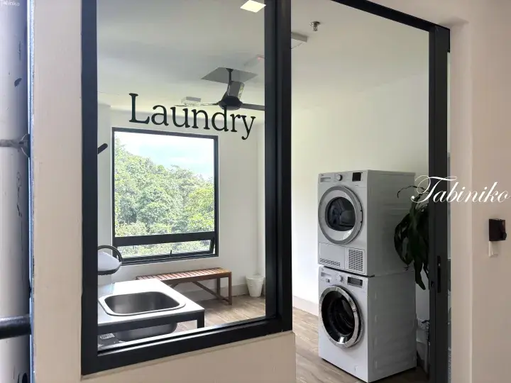 Modern laundry room with stacked washer and dryer, sink, and window view of greenery.