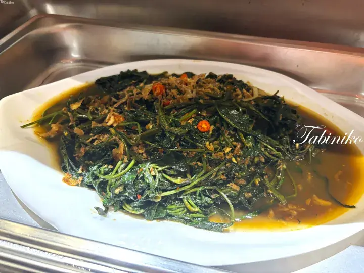 A plate of stir-fried spinach with garlic and chili in a savory sauce, served in a buffet tray.