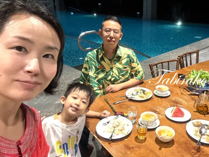 Family enjoying dinner by the pool at night with tropical decor and watermelon slices.