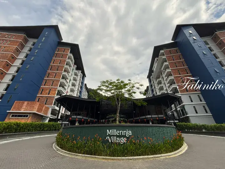 Millennia Village entrance with blue and brick buildings and a landscaped roundabout.