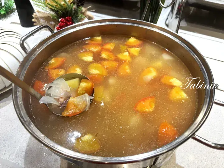 A steaming pot of clear soup with chunks of pumpkin and vegetables served in a buffet setting.