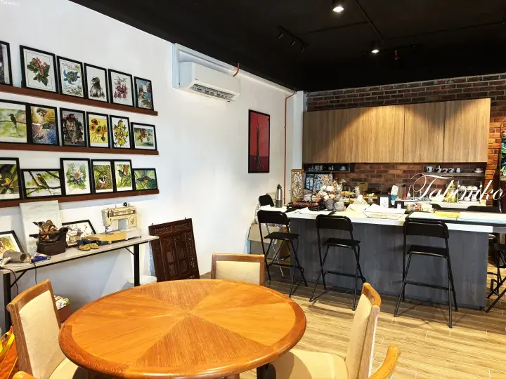 Cozy cafe interior with wooden tables, framed art on white walls, and a kitchen counter with stools.