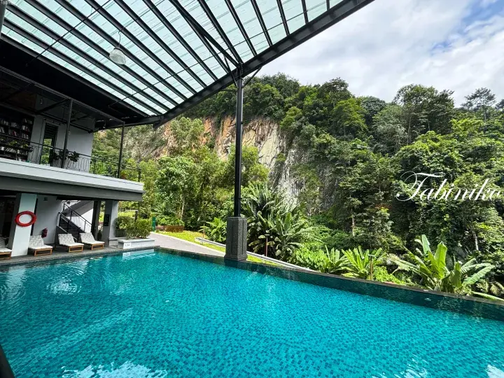 Infinity pool with glass roof overlooking lush tropical hillside and limestone cliff at a luxury resort.