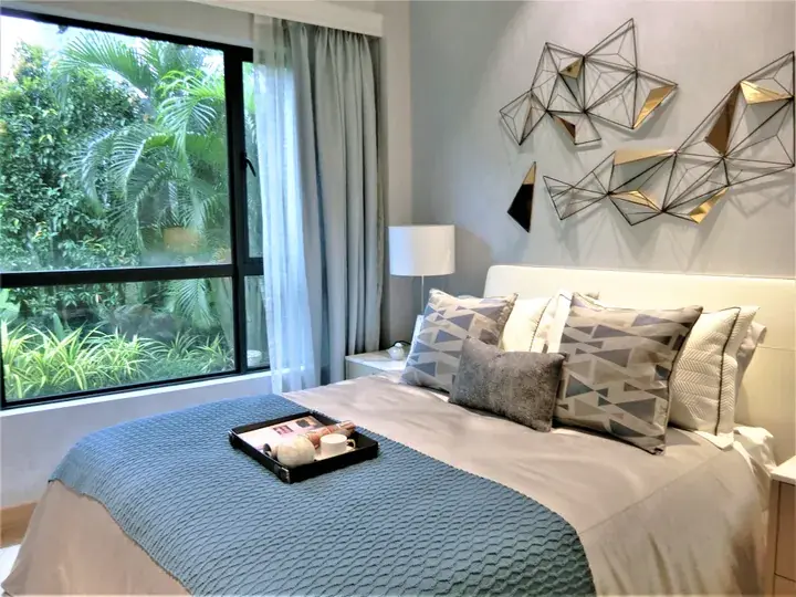 Modern bedroom with geometric wall art, patterned pillows, and a large window overlooking lush tropical greenery.