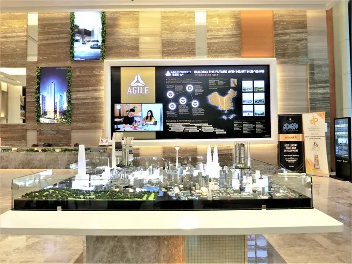Architectural model of a modern cityscape displayed at an Agile Property sales gallery with digital screens in the background.