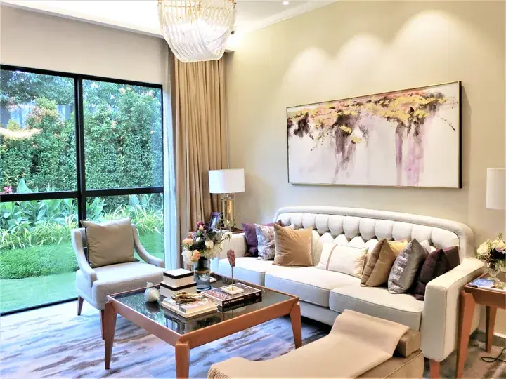 Bright living room with white sofa, abstract art, and large glass doors opening to a lush garden.