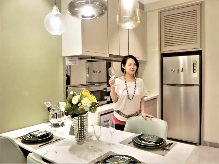 Woman holding wine glass in modern kitchen with stainless steel appliances and marble dining table.