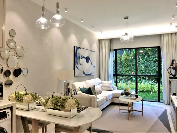 Modern living room with white sofa, abstract wall art, and large glass doors opening to a lush garden.
