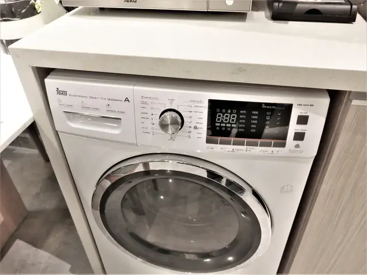 White Teka front-loading washing machine with digital display and control panel installed in a modern laundry space.