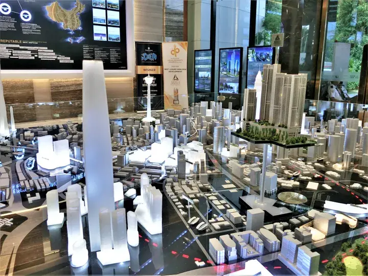 Detailed architectural model showcasing a modern high-rise development with surrounding urban landscape and digital displays.