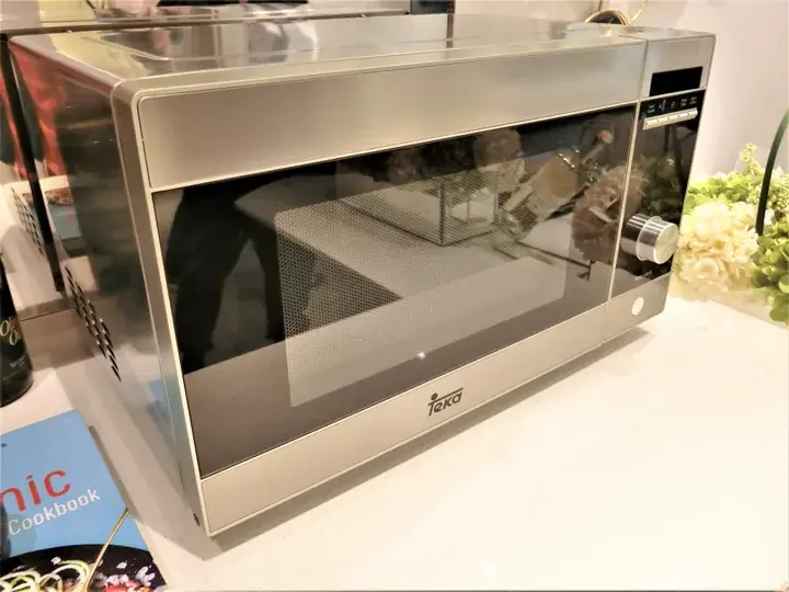 Teka stainless steel microwave oven with digital display and control knob on a white countertop.