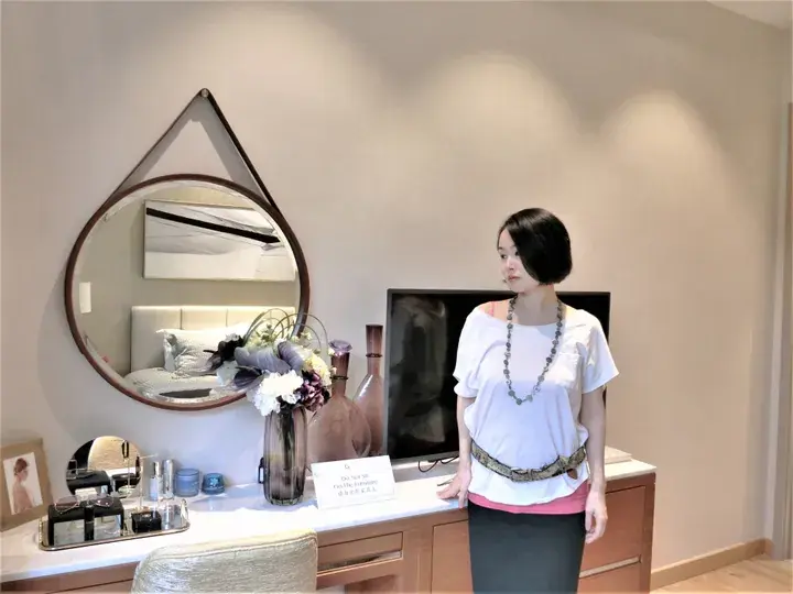 Woman in a modern hotel room beside a vanity mirror and TV, showcasing stylish interior design.