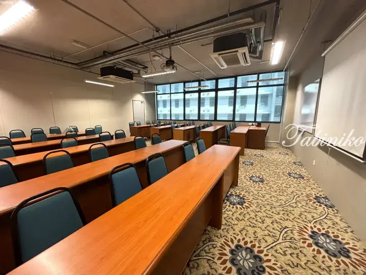 Modern conference room with wooden tables, blue chairs, and large windows overlooking a city building.