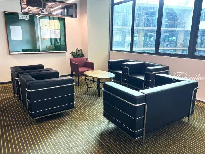 Modern lounge area with black leather sofas and a red armchair near large windows overlooking a city view.