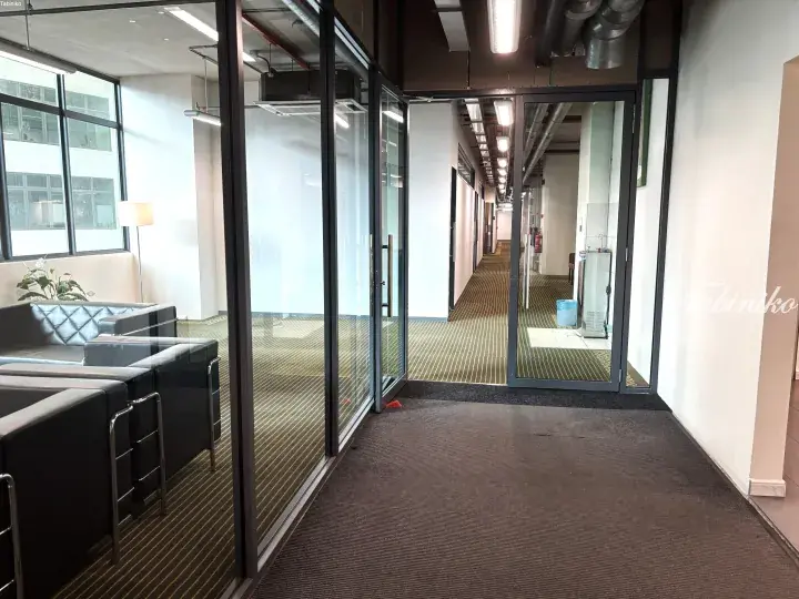 Modern office interior with glass-walled meeting rooms and a long hallway featuring industrial-style exposed ceiling pipes.