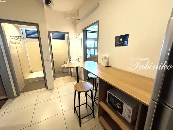 Modern hostel kitchenette with wooden counter, bar stools, microwave, and separate shower and toilet rooms.