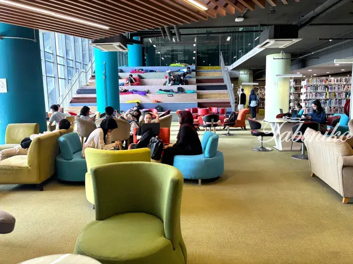 Students studying in a modern library with colorful tiered seating and comfortable lounge chairs.