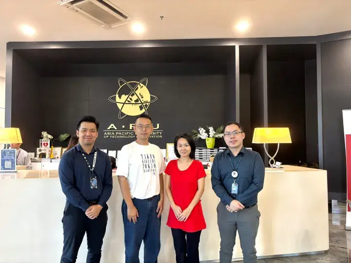 Four people standing in front of the Asia Pacific University of Technology & Innovation reception desk.