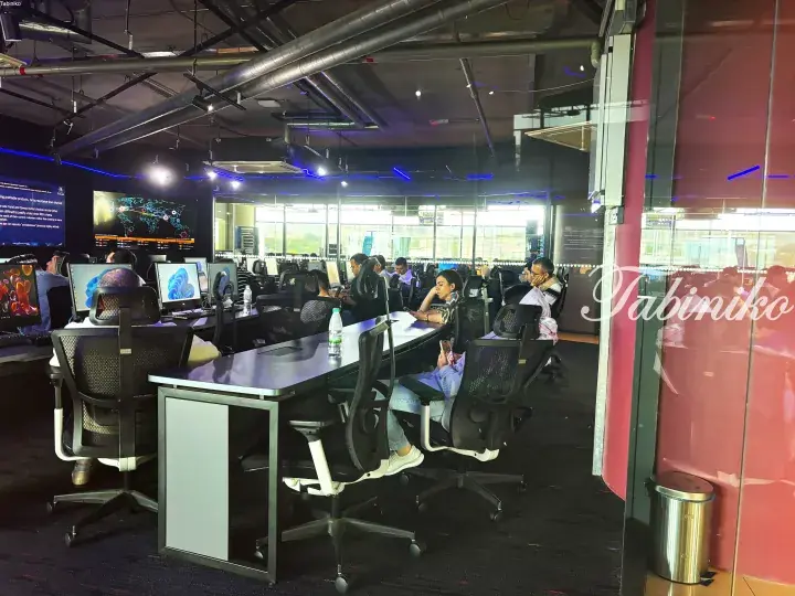 Modern office interior with employees working at desks and large display screens on the wall.