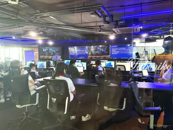 Students in a modern computer lab with large screens displaying world maps and data dashboards.