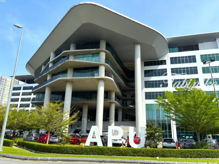 Modern APU building exterior with large white letters and parked cars in front.