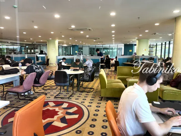 Students studying in a modern library with colorful chairs and a large Malaysian flag carpet design.