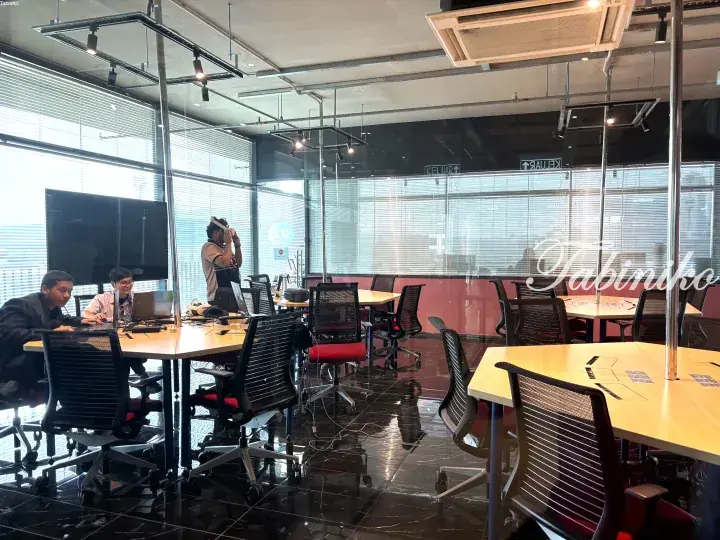 Modern co-working space with wooden tables, black chairs, and glass walls where people work and take photos.